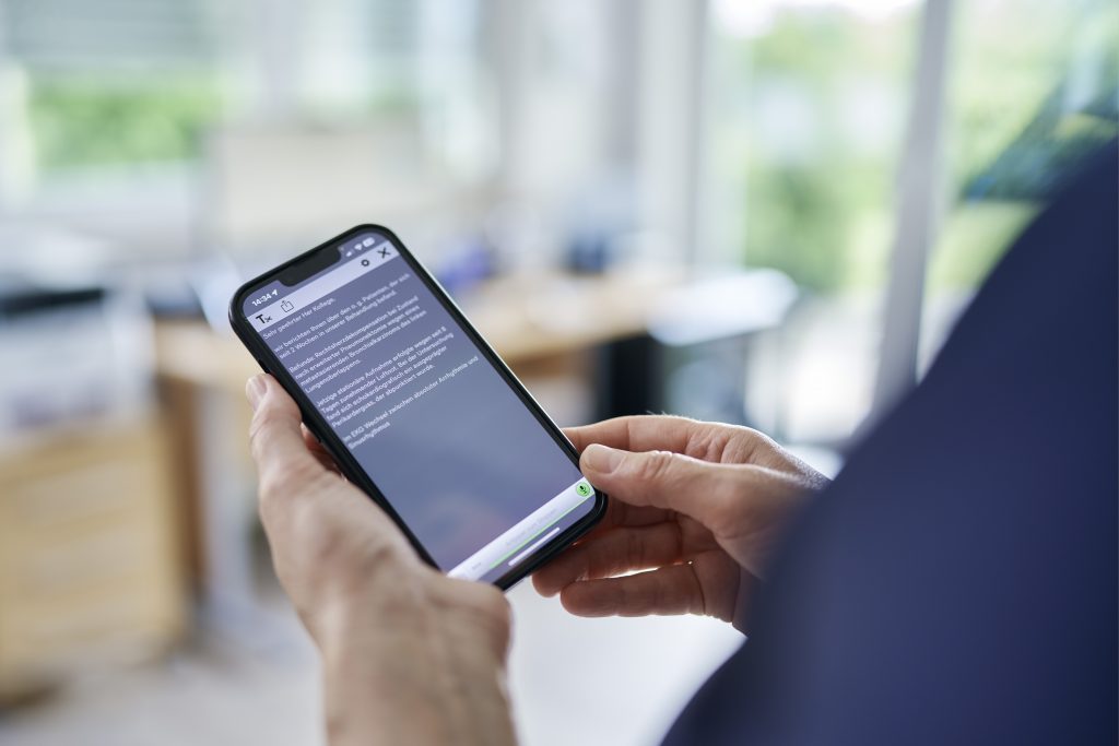 Eine Person mit Smartphone, auf dem ein langer Text angezeigt wird, der mithilfe der Solventum™ Fluency Direct App per Spracheingabe erstellt wurde.